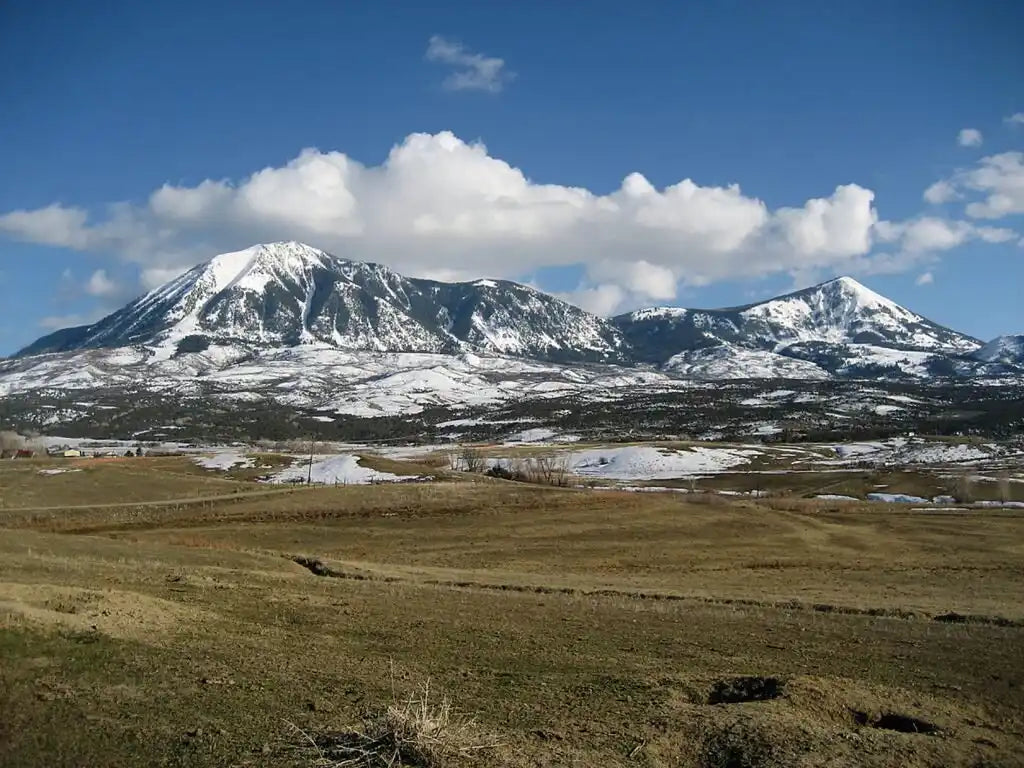 Snow-capped mountain range with rugged peaks and patches of green grass in the foreground.
