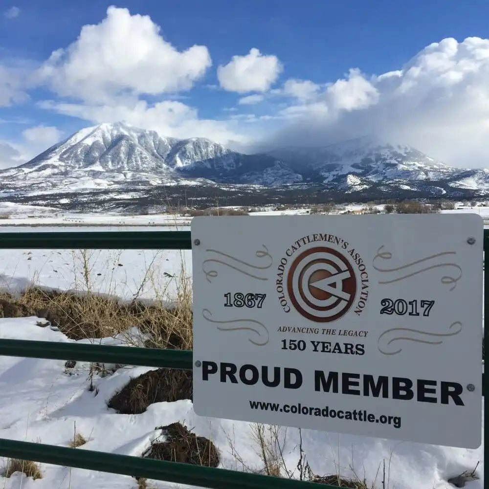 White sign with black text and logo, mounted on a metal fence.