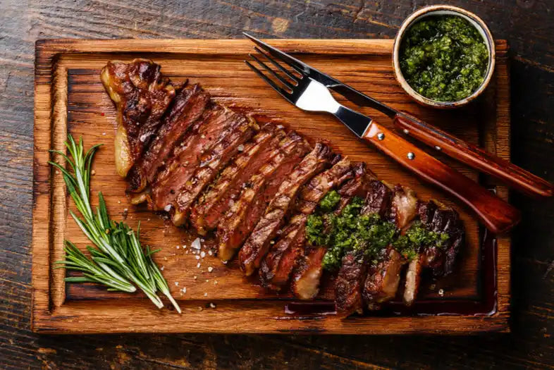 Wooden cutting board with grilled ribs and herbs.